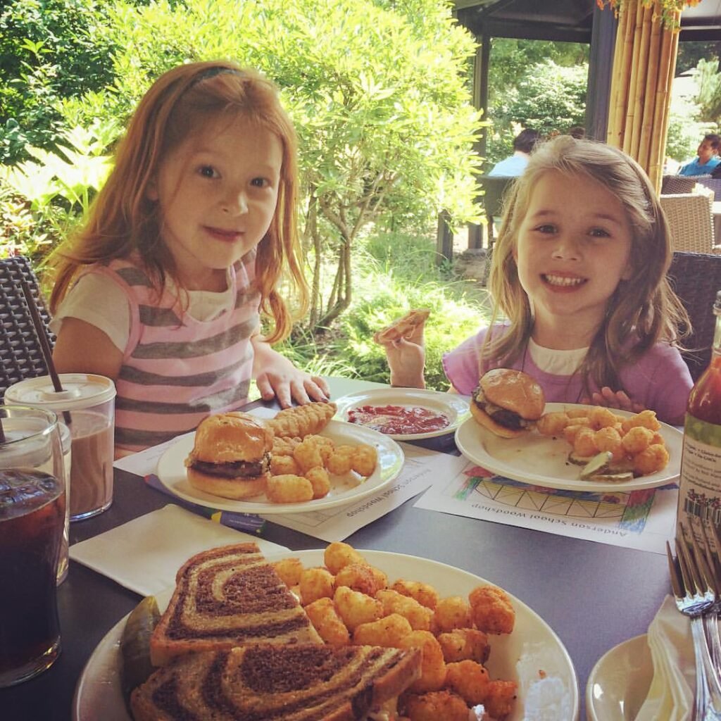 Children enjoying a meal outside, featuring sliders, tater tots, and sweet tea in a garden setting. A close-up view of a plate with lunch items on a table.