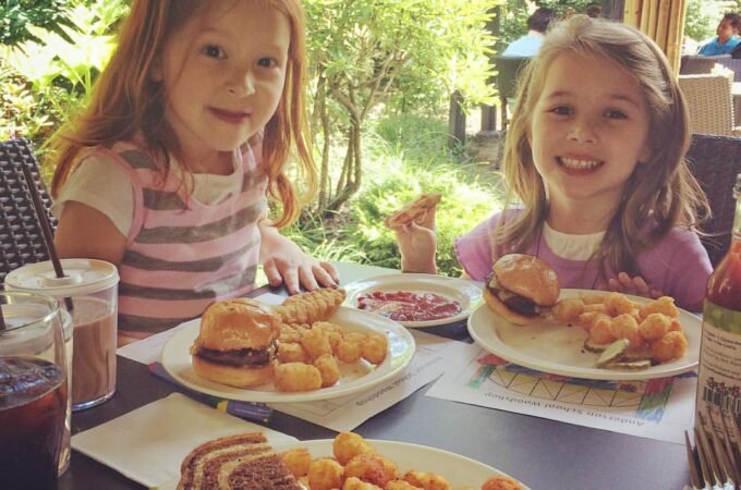 Children enjoying a meal outside, featuring sliders, tater tots, and sweet tea in a garden setting. A close-up view of a plate with lunch items on a table.