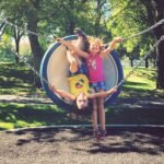 Children having fun on a circular swing in a park surrounded by trees.