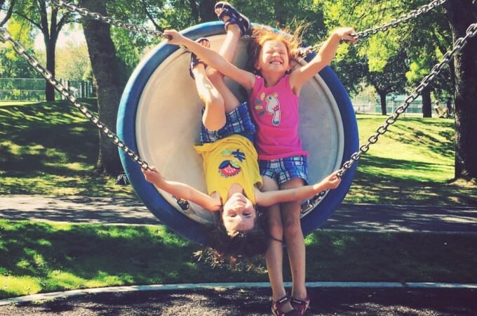 Children having fun on a circular swing in a park surrounded by trees.