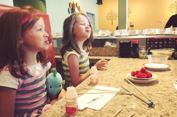 Two girls at a sushi bar counter with chopsticks and plates of food at the Maki Spot in Portland.