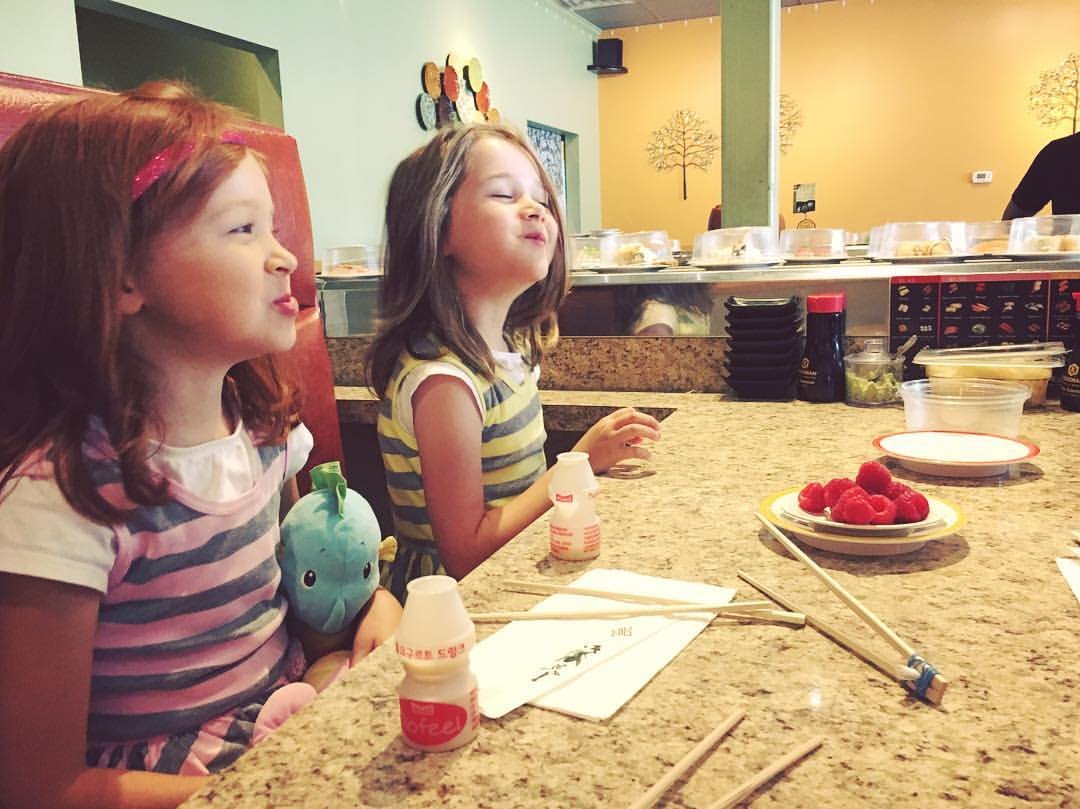 Two girls at a sushi bar counter with chopsticks and plates of food at the Maki Spot in Portland.
