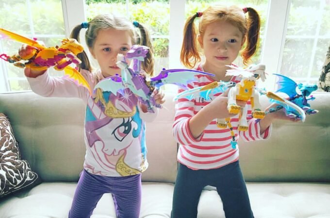 Two young children play with colorful LEGO Dragon toys on a couch in a bright, sunny room.