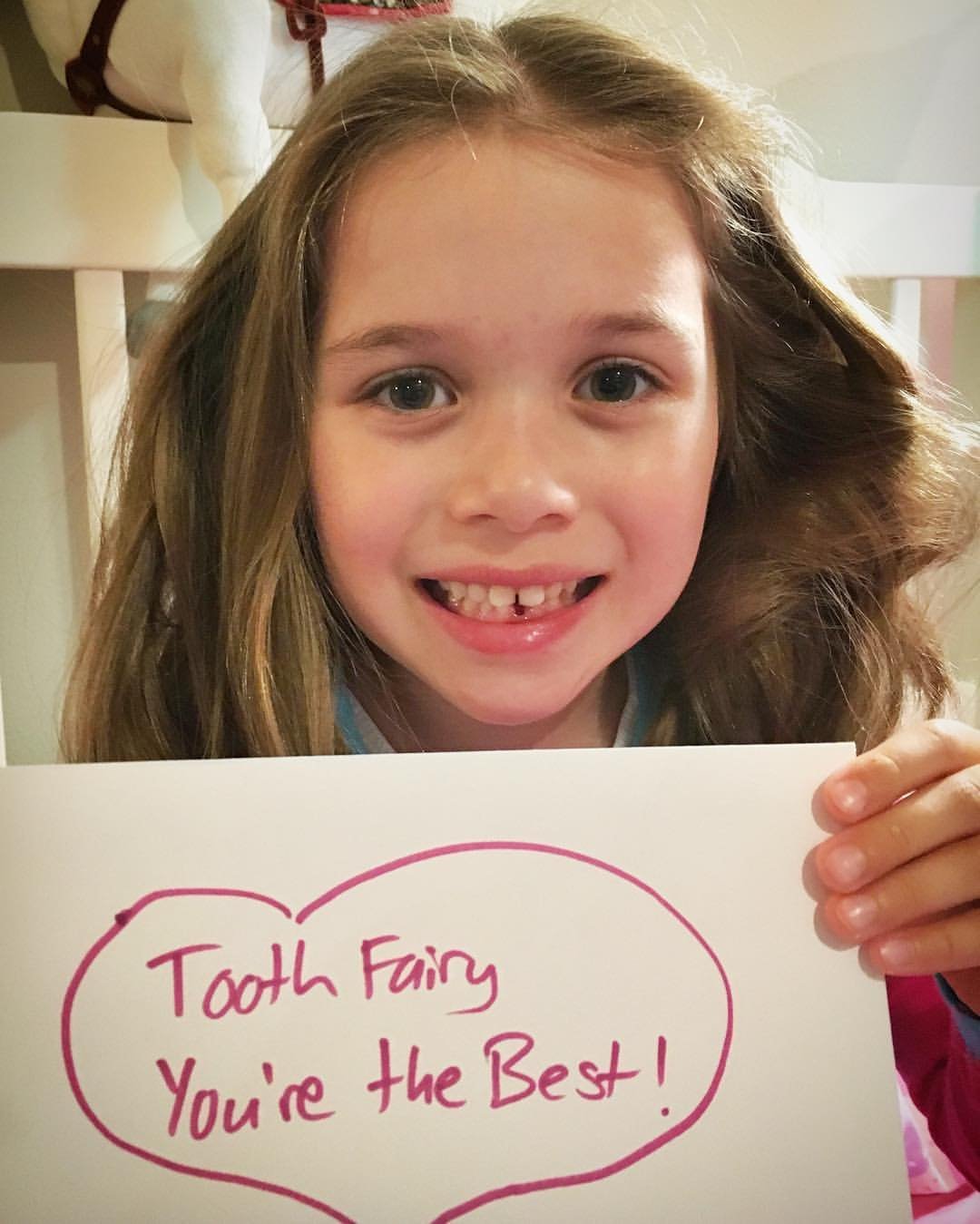 Fellow Tooth Fairies A smiling child holds a handmade sign reading 'Tooth Fairy You're the Best!' after losing their first baby tooth.