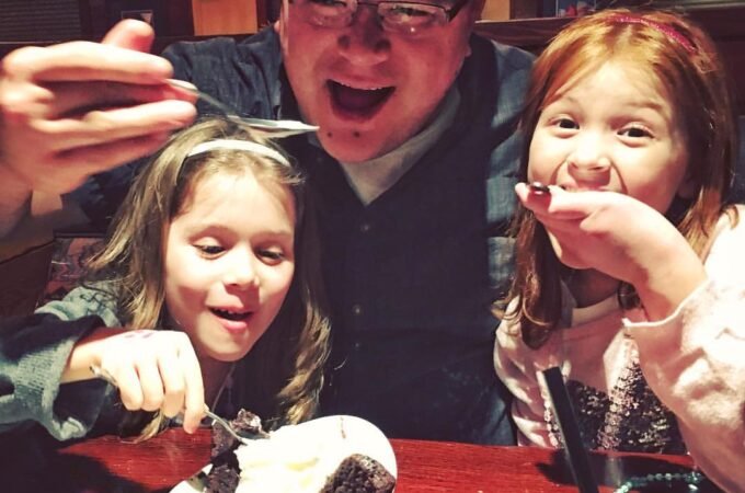 A delighted group shares a treat at a restaurant, laughing over a dessert bowl at a red table.