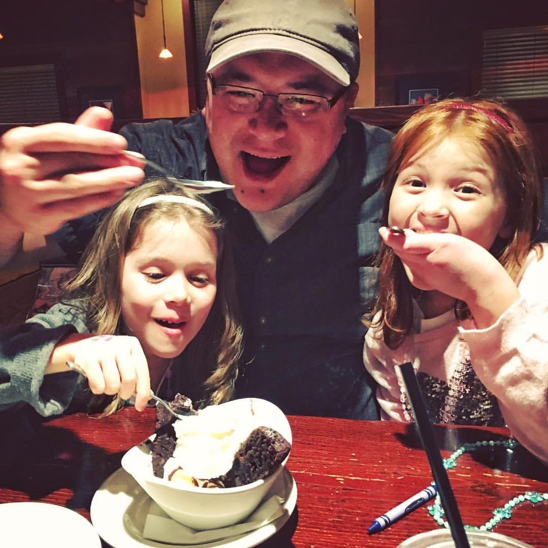 A delighted group shares a treat at a restaurant, laughing over a dessert bowl at a red table.