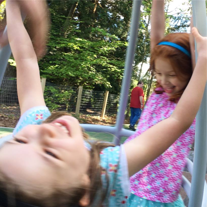 Two children play on a swing set in a sunny park.