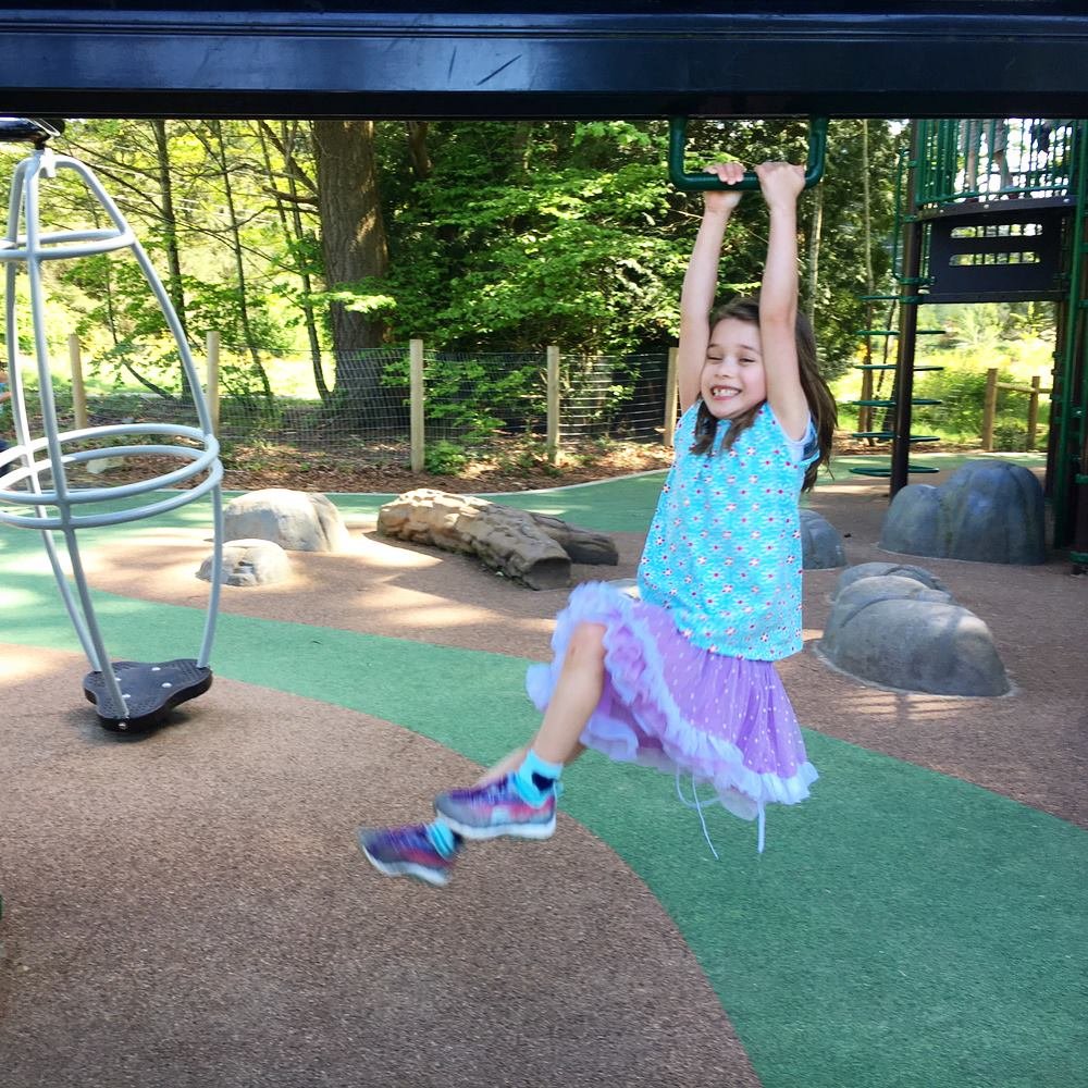 A child on a monkey bar at a sunny park playground.