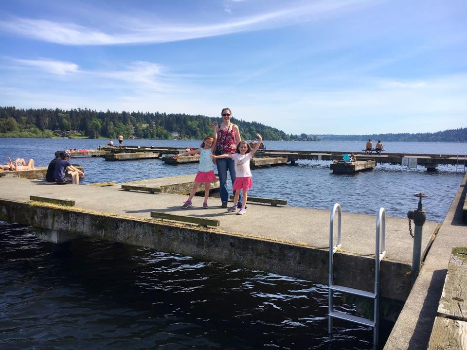 A cheerful group poses on a concrete lake dock with a forested shoreline in the background.