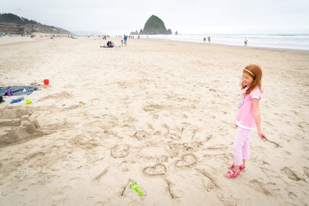 A joyful summer day at a Pacific Northwest beach featuring playful sand art and a child exploring the shoreline.