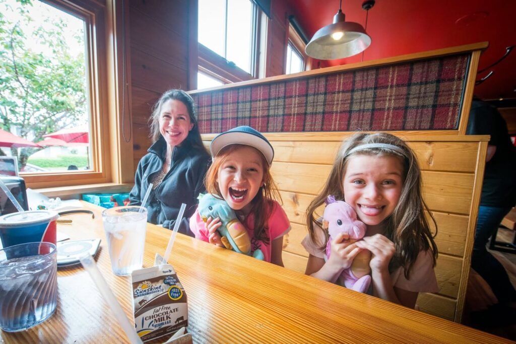 A smiling family enjoys a meal together in a charming wooden restaurant booth with plaid accents.