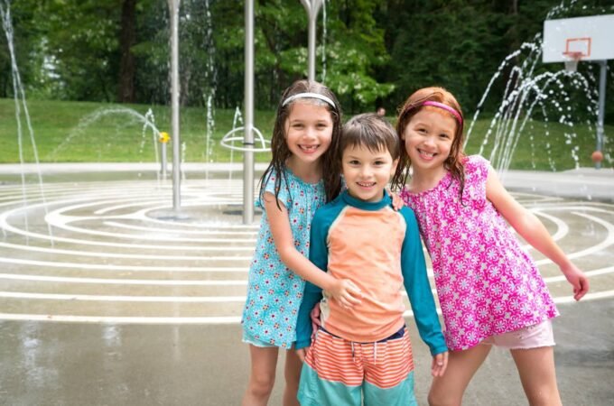 Three children posing in a park spray fountain on a sunny day.