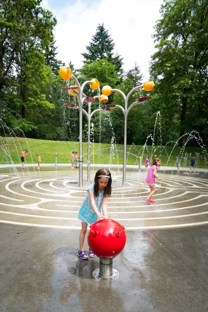A playful scene at the Bloom Quarter sculpture fountain in Portland, Oregon, where visitors cool off under the interactive water jets and colorful floral sculptures.