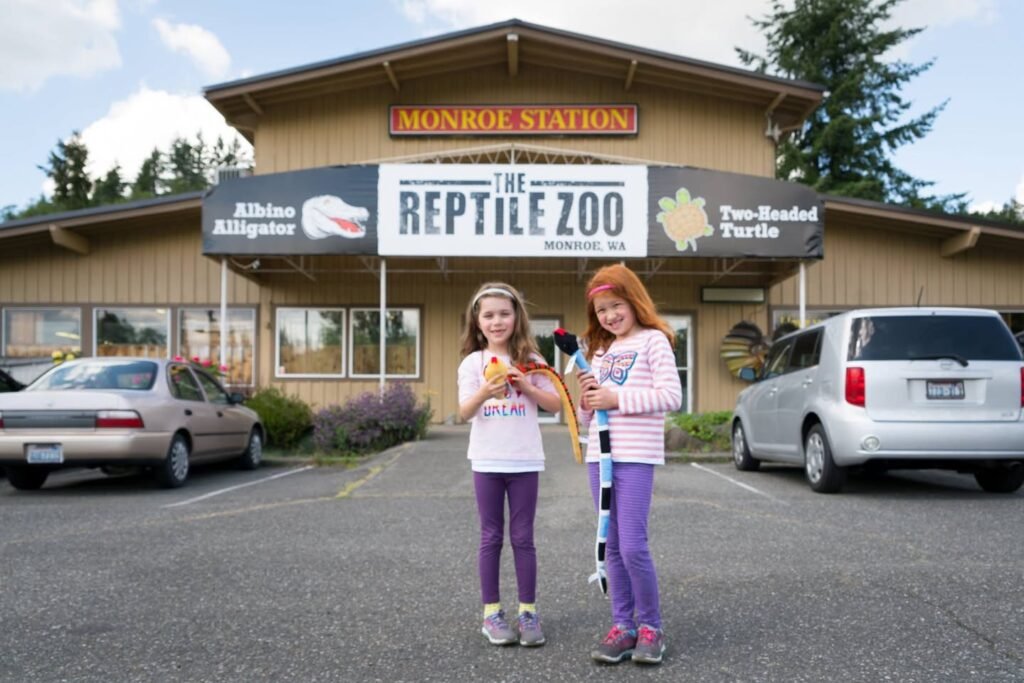 Two people holding snakes in front of The Reptile Zoo building.