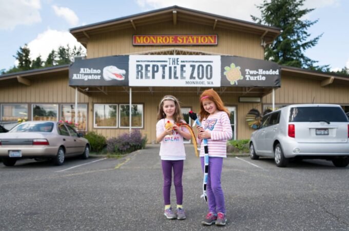 Two people holding snakes in front of The Reptile Zoo building.