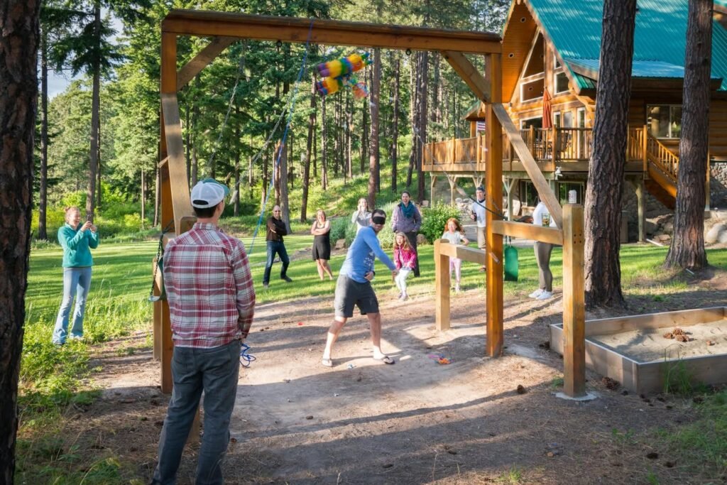 People playing ax throwing at a resort with wooden structures and forest scenery.