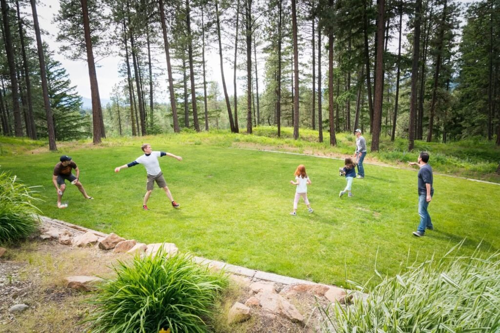 A family playing a game in a lush grassy clearing surrounded by tall pine trees.