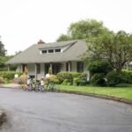 Bicycles parked in front of a single-story home in the Pacific Northwest, featuring lush gardens and mature trees.
