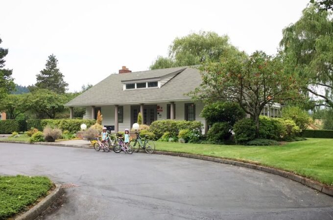 Bicycles parked in front of a single-story home in the Pacific Northwest, featuring lush gardens and mature trees.