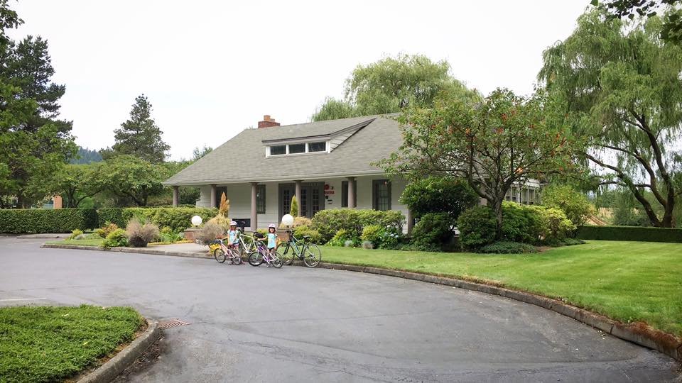 Bicycles parked in front of a single-story home in the Pacific Northwest, featuring lush gardens and mature trees.