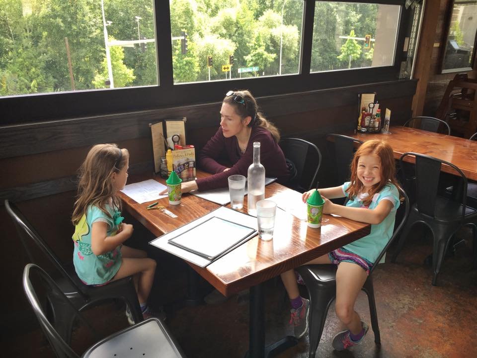 A woman and two girls sitting at a table in a restaurant with a view of greenery.
