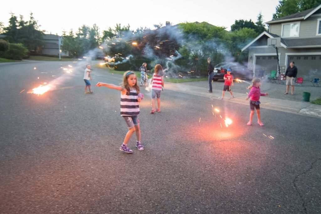 Children enjoying a night of safe summer fireworks in a quiet suburban neighborhood. Bright sparks and smoke fill the evening air.
