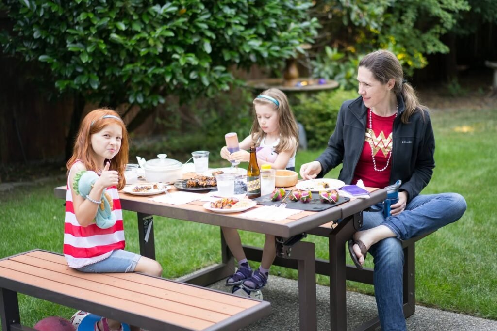 A family enjoys a refreshing meal at an outdoor wooden table surrounded by a lush green garden in the Pacific Northwest.