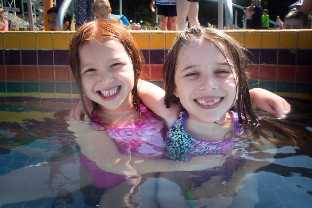 Two smiling individuals posing together in a colorful pool, wearing vibrant swimwear while enjoying a sunny day.