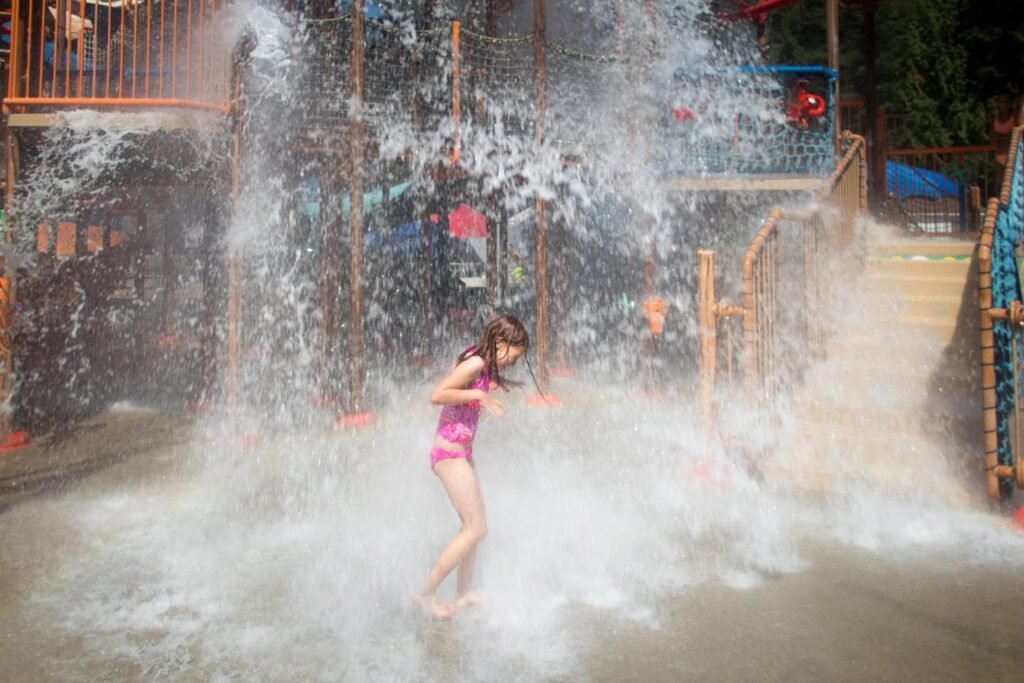 A person in a pink swimsuit playing in a water park fountain area with water spraying from above.