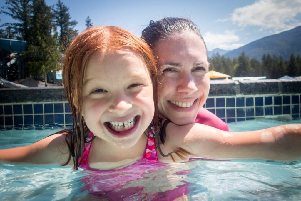 Two individuals smiling happily in an outdoor swimming pool with a scenic mountain backdrop.