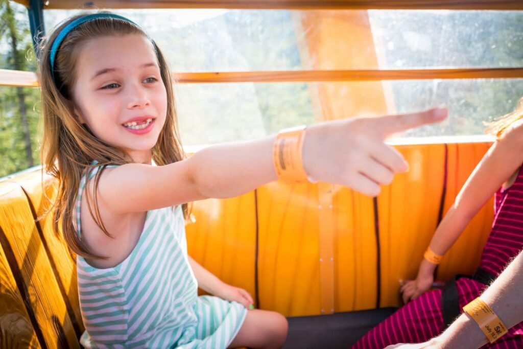 A young person seated on a ride points enthusiastically toward something outside the window during a fun excursion.