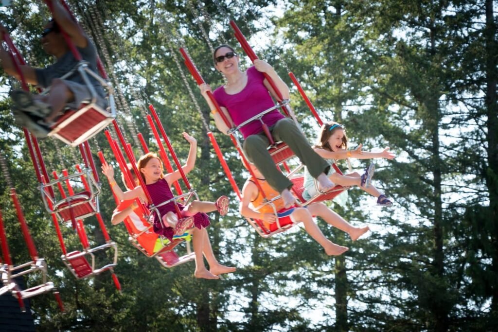 Riders on a swinging amusement park ride set against a backdrop of tall trees.
