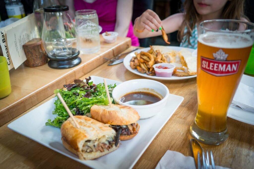 A plate of sandwiches and onion rings served with a Sleeman beer at a casual restaurant.