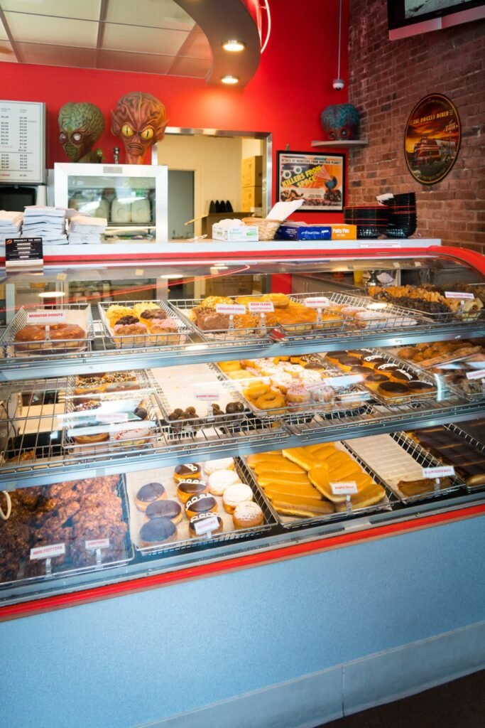 A bakery display case filled with various pastries and baked goods against a red wall in a local shop.