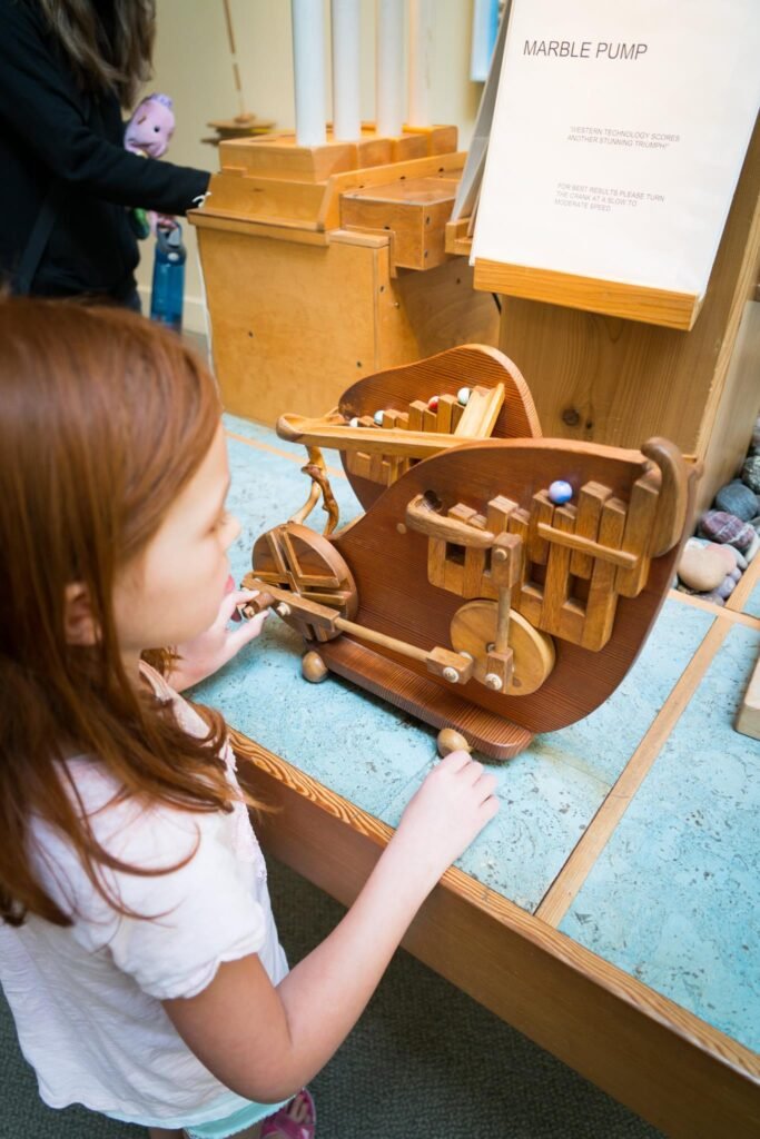 A child using a wooden marble pump display. The setup includes a detailed information board.