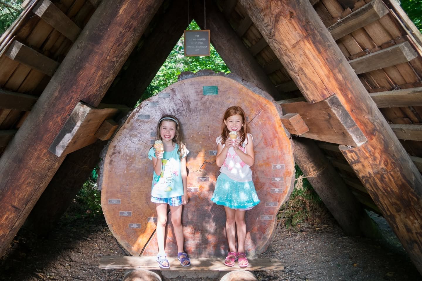 Northwest Trek Two children stand under a rustic wooden A-frame structure with a circular cutout background.