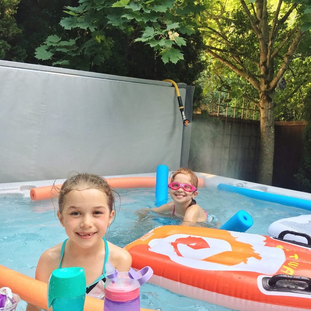 Children enjoying a swim in an above-ground pool surrounded by green foliage.
