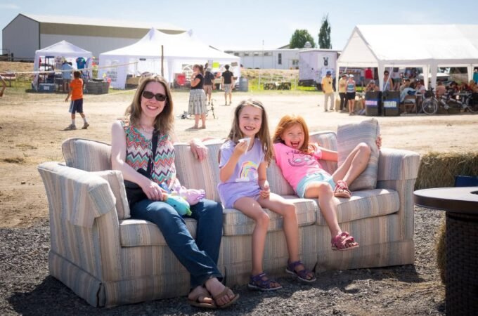 A collage of photos from a farm stand visit, showing people relaxing on a couch in a rural setting with white tents in the background. The images capture a casual, sunny day at a local farm market.
