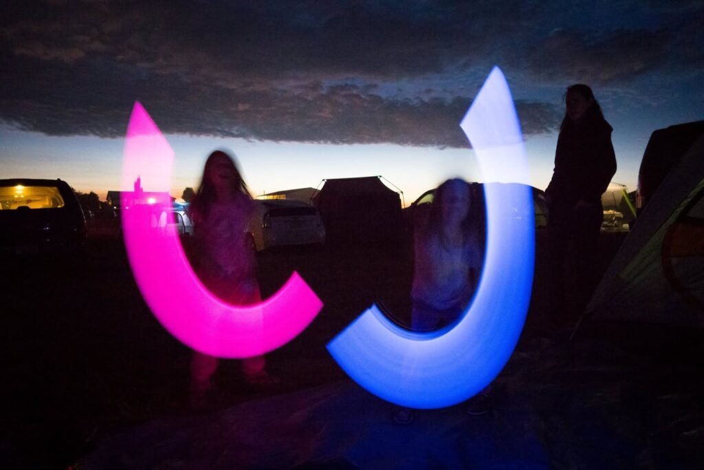 Vibrant pink and blue illuminated cups held aloft by people during a nighttime outdoor event under a dusk sky.