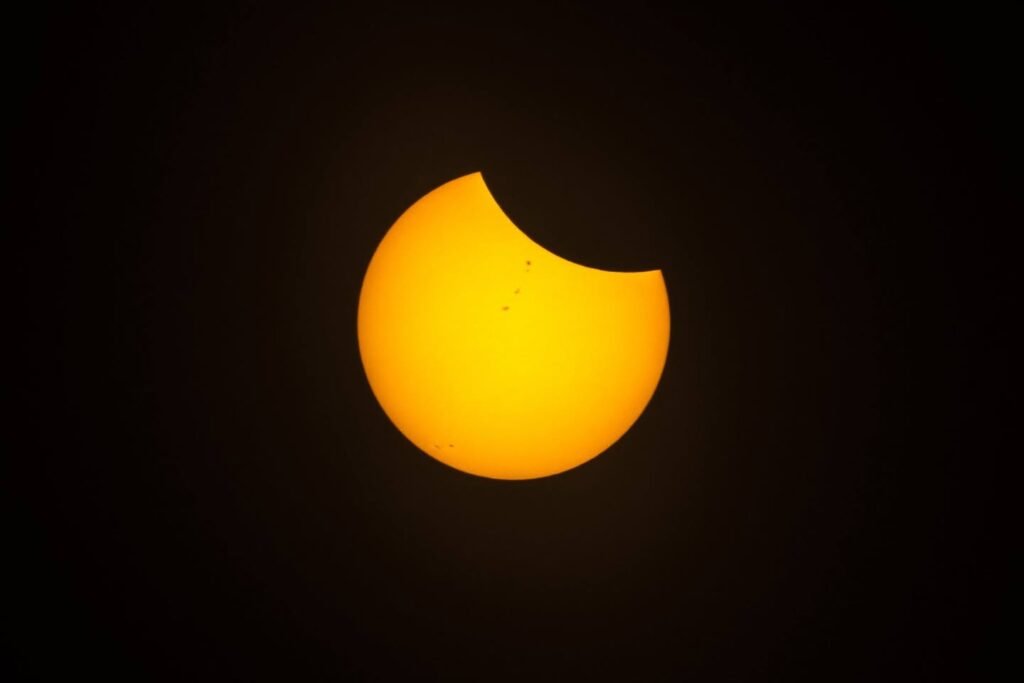 A glowing golden sun is partially covered by the moon, creating a distinct crescent shape against a dark background. This close-up view emphasizes the bright colors of a solar event.
