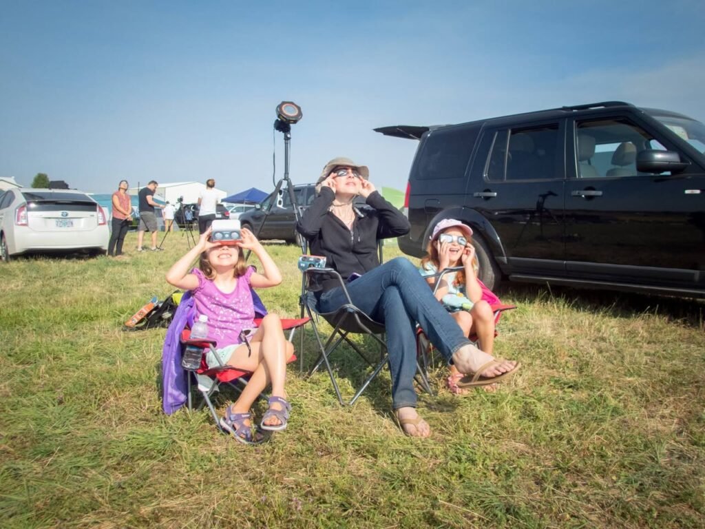 A family relaxing on the lawn in camping chairs near parked SUVs under a clear blue sky.