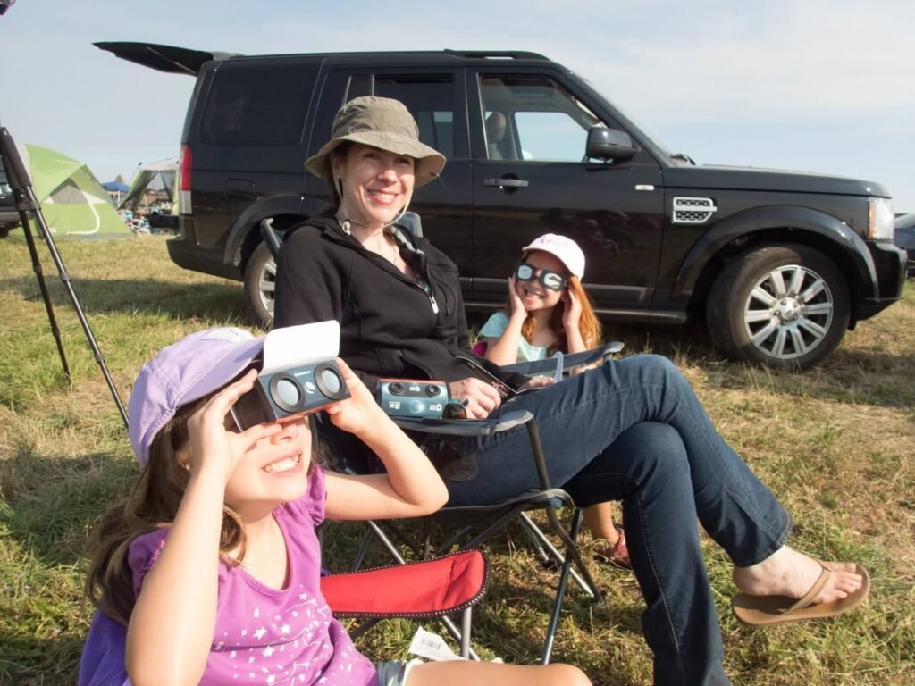 Family members enjoy the night sky with binoculars at a campsite near their vehicle.