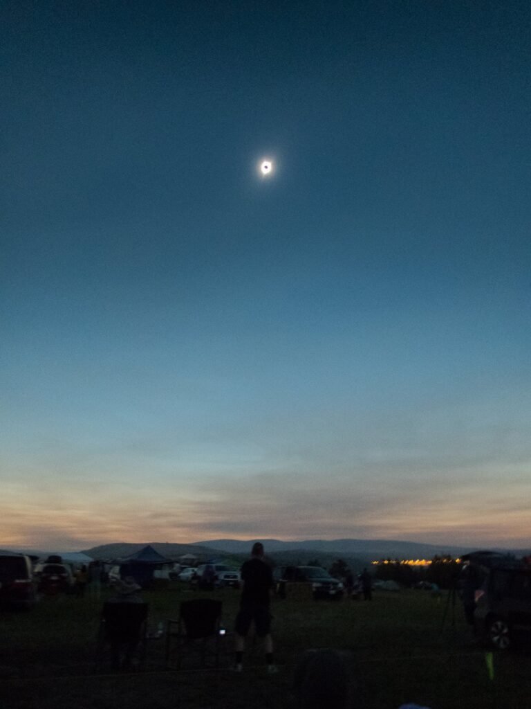 A view of a full moon rising over a distant cityscape during late dusk at a campsite in the Pacific Northwest.