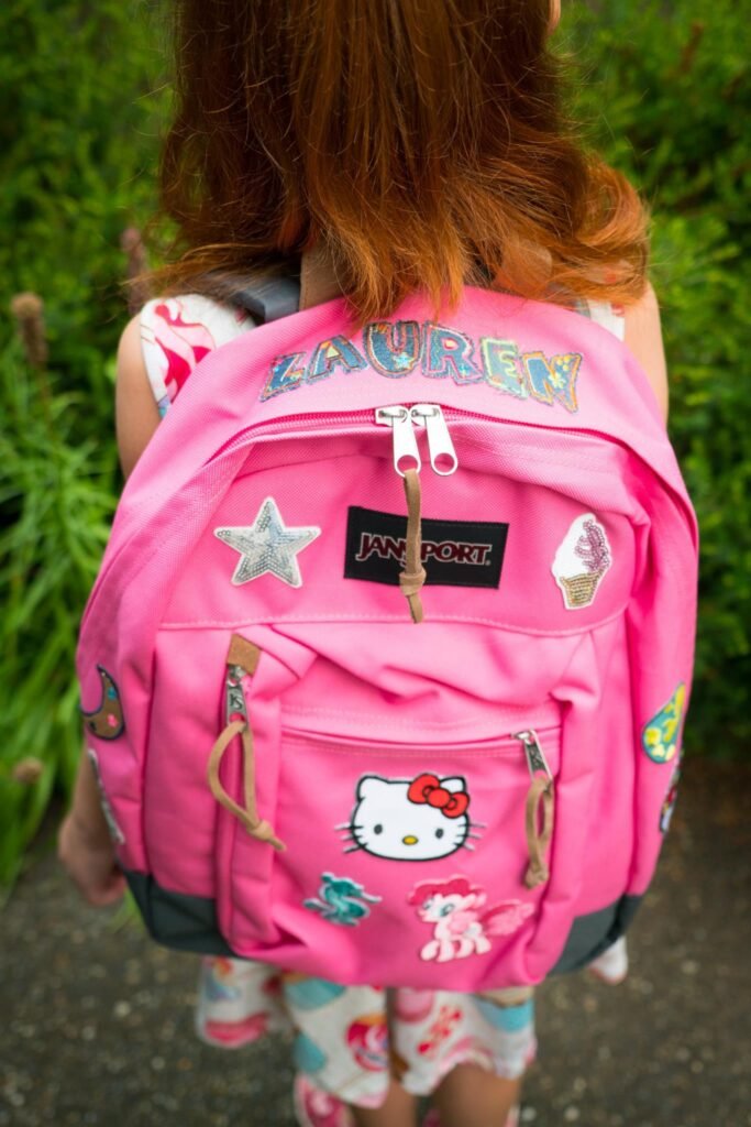 A person wearing a pink backpack decorated with Hello Kitty logos and the name Lauren.