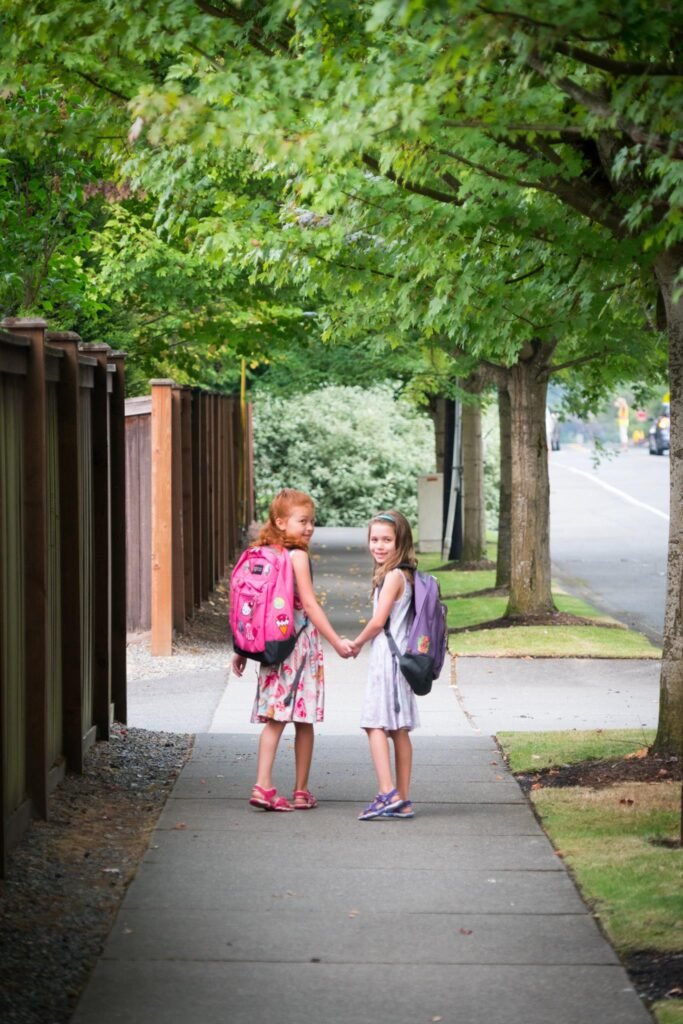 Two children holding hands while walking along a tree-lined sidewalk.