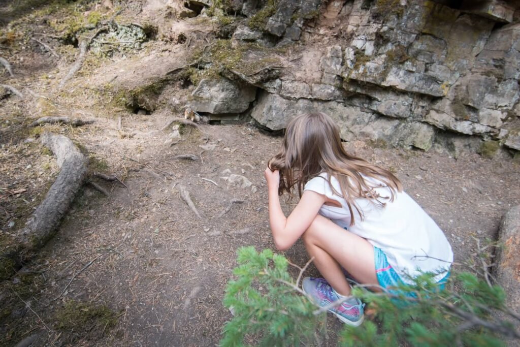 A hiker crouches near a mossy rock wall on a forest trail.
