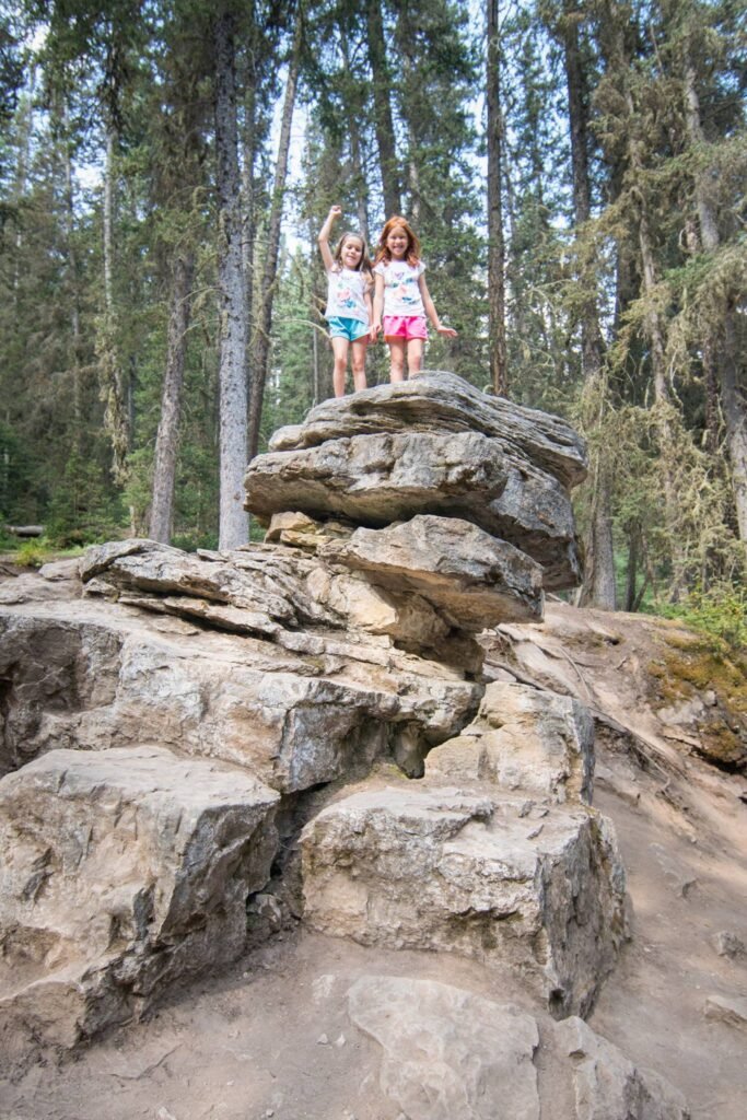 Children explore large boulders on a rugged hiking trail in the Pacific Northwest forest.