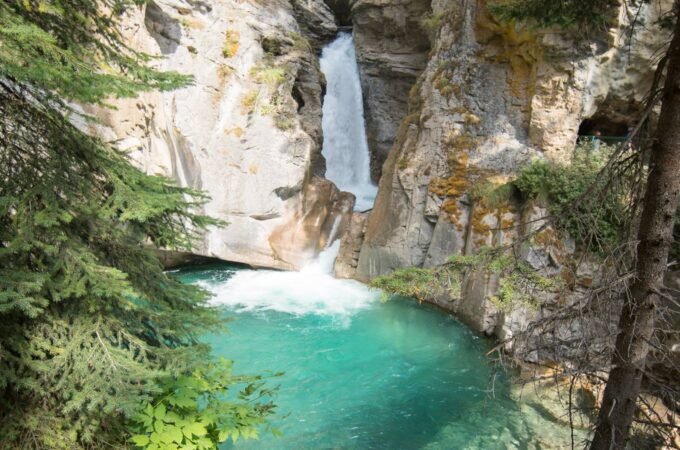 A scenic view of a waterfall flowing into a vibrant turquoise pool surrounded by rocky cliffs and lush green trees.