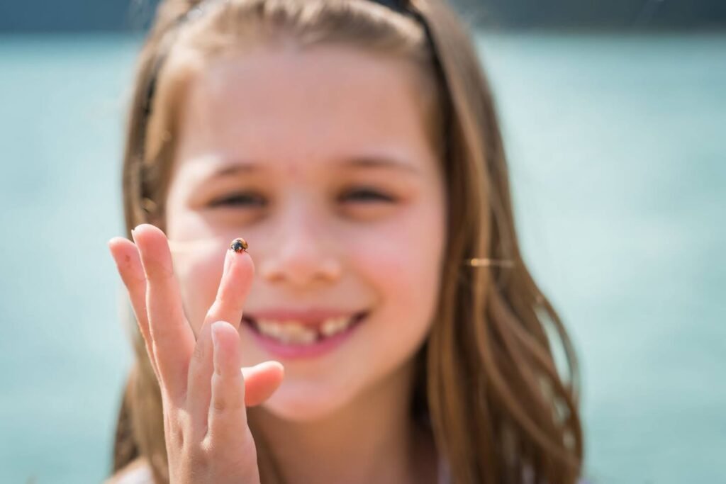A close-up view of a happy child with long brown hair smiling so near a body of water in the bright daylight.