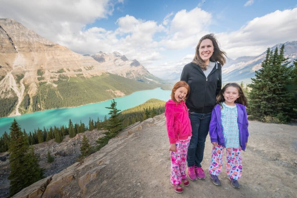 A family standing on a rocky outcropping overlooking the turquoise waters of Moraine Lake in Canada, with the Valley of the Ten Peaks in the background.
